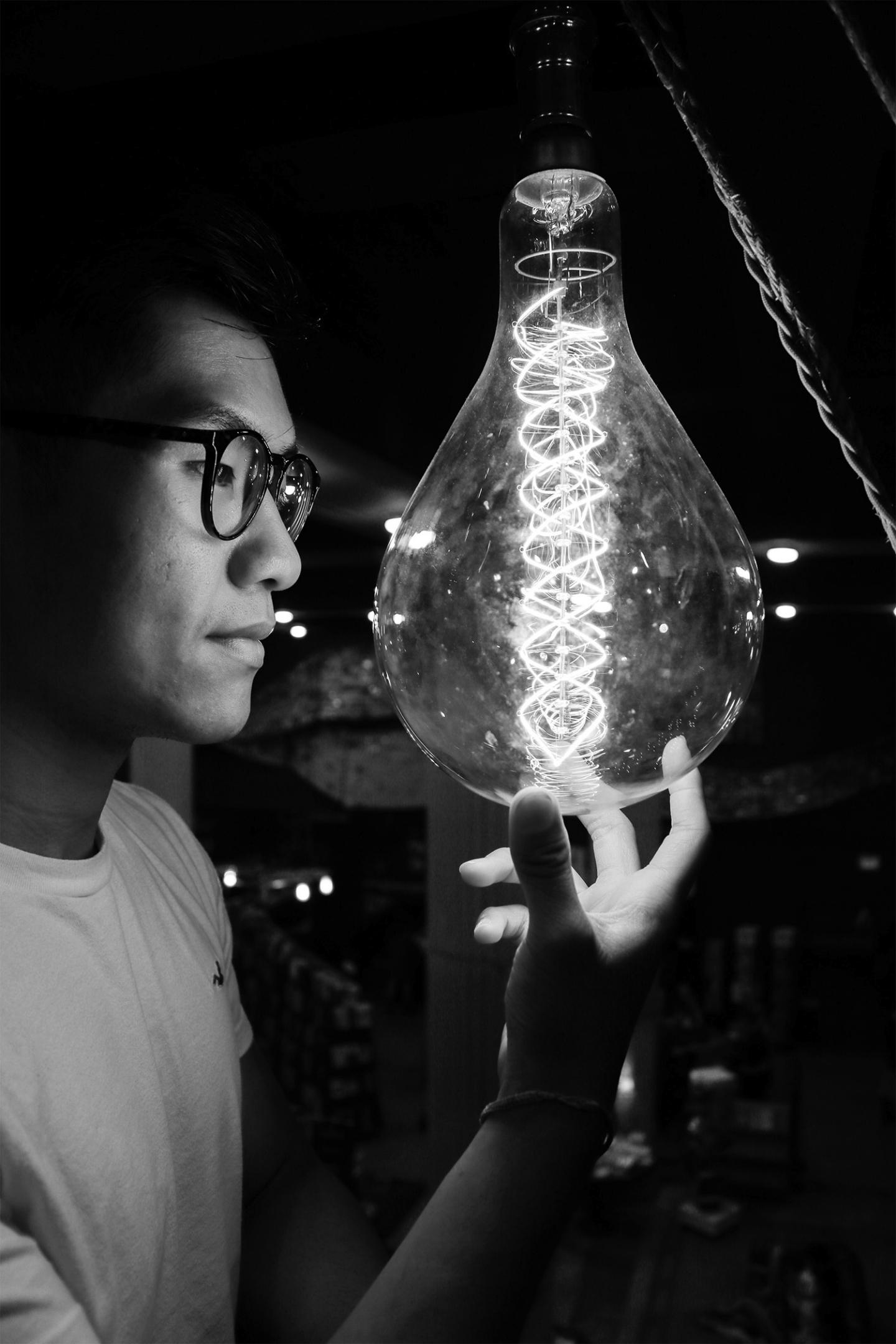 A man closely observing a large lightbulb in a dark studio.