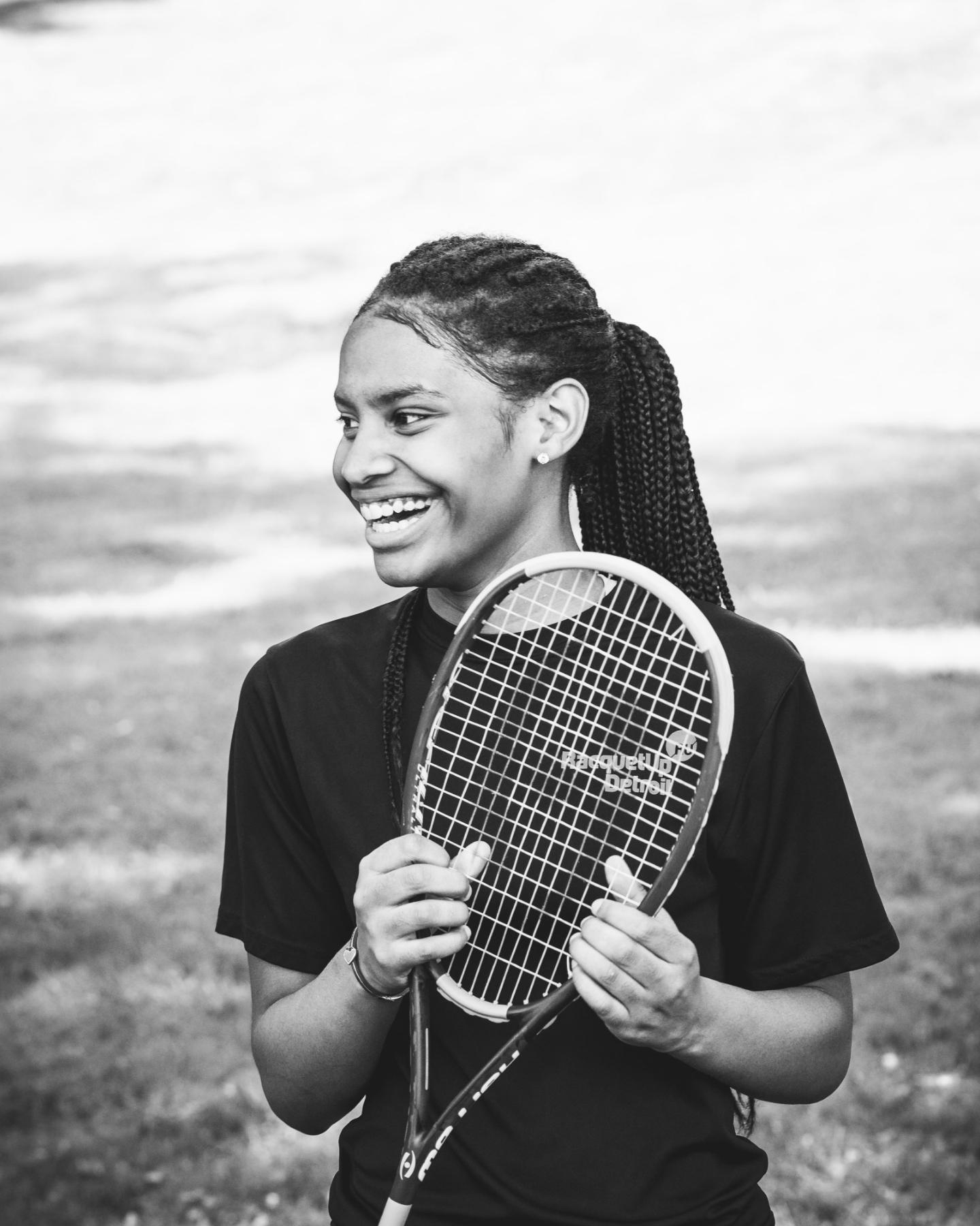 A young girl with a pony tail, holding a racquet.